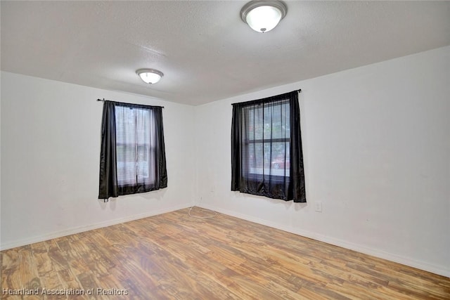 empty room with a wealth of natural light, a textured ceiling, and hardwood / wood-style flooring