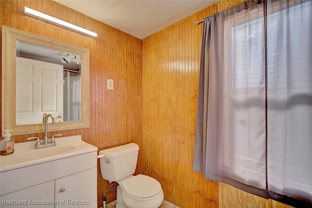 bathroom with vanity, wood walls, and toilet