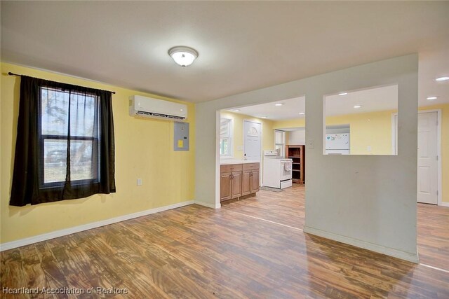 unfurnished room with a wall unit AC, washer / clothes dryer, electric panel, and light hardwood / wood-style floors