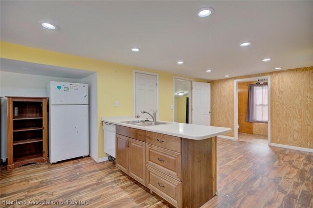 kitchen with sink, light hardwood / wood-style floors, white appliances, wooden walls, and a center island with sink