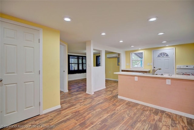 kitchen with a wall unit AC, hardwood / wood-style flooring, sink, and range