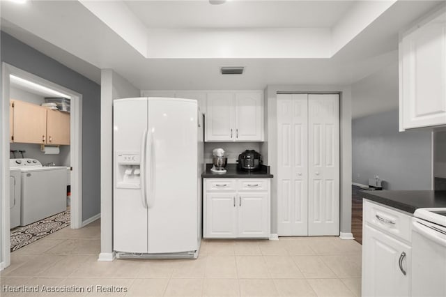 kitchen featuring a raised ceiling, washer and dryer, light tile patterned floors, white cabinetry, and white fridge with ice dispenser