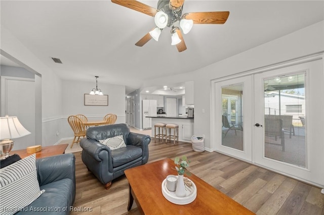 living room with ceiling fan with notable chandelier, light hardwood / wood-style flooring, and french doors