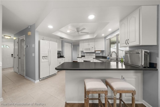 kitchen featuring white cabinetry, a raised ceiling, kitchen peninsula, white appliances, and a breakfast bar area