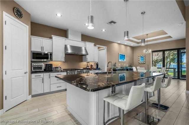500 Heartland Blvd, Lake Placid, FL 33852 - kitchen with wall chimney range hood, a sink, stainless steel microwave, a center island with sink, and white cabinets