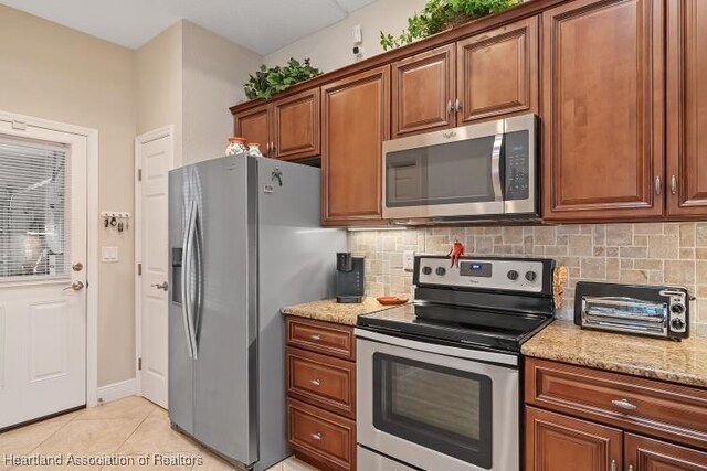 1624 Marble St, Sebring, FL 33870 - kitchen featuring appliances with stainless steel finishes, tasteful backsplash, light stone countertops, light tile patterned floors, and brown cabinetry