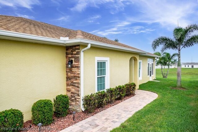 1624 Marble St, Sebring, FL 33870 - view of side of home with stucco siding, stone siding, a lawn, and a shingled roof