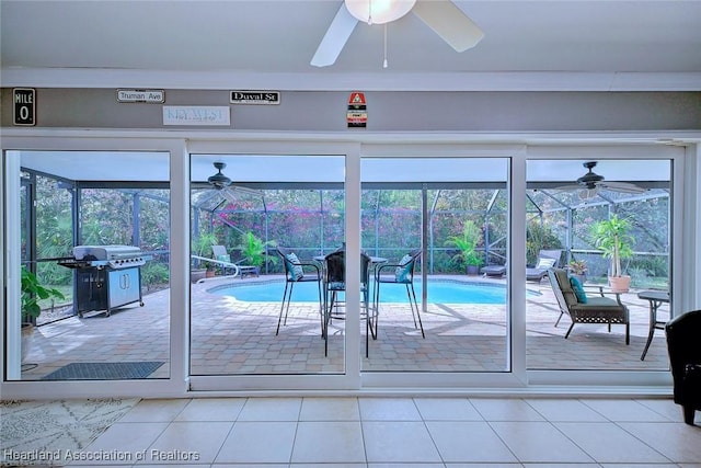 doorway to outside featuring a sunroom, a ceiling fan, and light tile patterned flooring