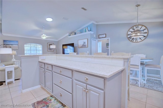 kitchen with light tile patterned floors, open floor plan, vaulted ceiling, light stone countertops, and crown molding