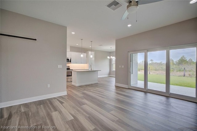 unfurnished living room featuring sink, ceiling fan with notable chandelier, a barn door, and light hardwood / wood-style flooring