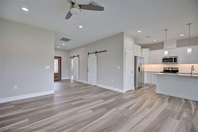 kitchen with light hardwood / wood-style flooring, appliances with stainless steel finishes, decorative light fixtures, white cabinets, and a barn door