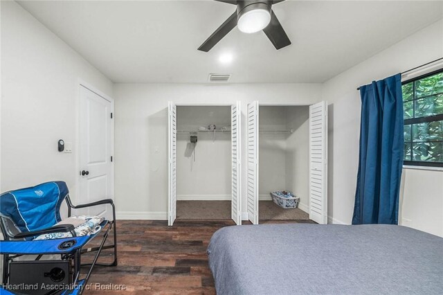 bedroom featuring ceiling fan, wood finished floors, visible vents, baseboards, and multiple closets