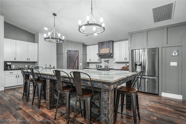 kitchen with visible vents, decorative backsplash, dark wood-style floors, wall chimney exhaust hood, and stainless steel fridge