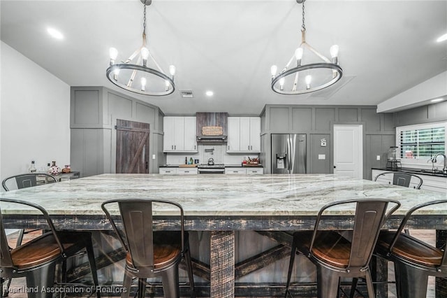 kitchen featuring a breakfast bar area, appliances with stainless steel finishes, light stone counters, vaulted ceiling, and a chandelier