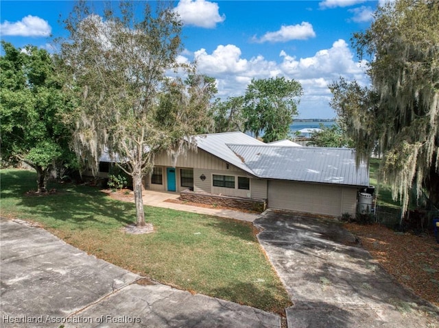 ranch-style home featuring a garage, a front yard, concrete driveway, and metal roof