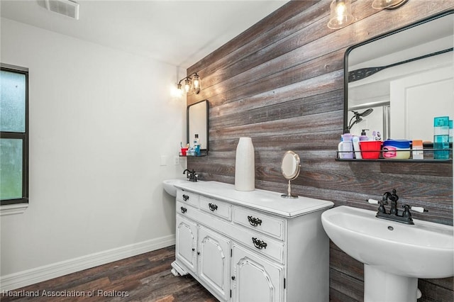 bathroom with visible vents, a sink, wooden walls, wood finished floors, and baseboards