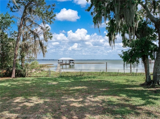 view of yard with a dock, a water view, fence, and boat lift