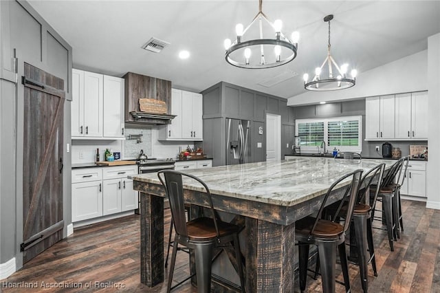 kitchen featuring a notable chandelier, a breakfast bar area, visible vents, appliances with stainless steel finishes, and premium range hood