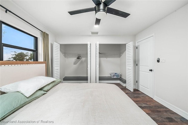 bedroom with wood finished floors, visible vents, a ceiling fan, baseboards, and two closets