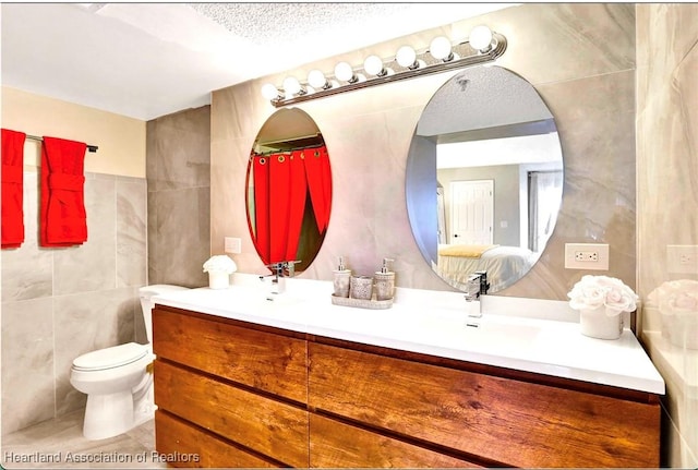 bathroom featuring a textured ceiling, vanity, toilet, and tile walls