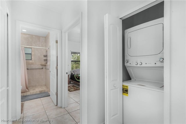 laundry area with stacked washer / drying machine and light tile patterned flooring