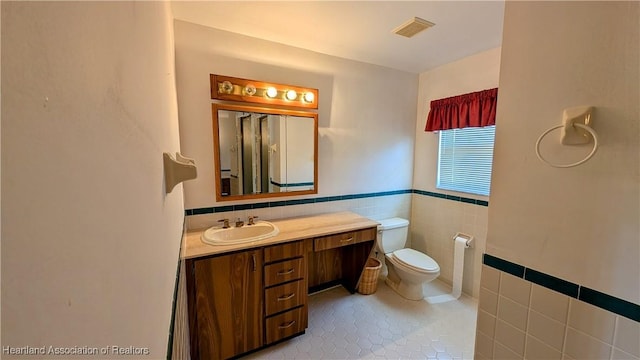 bathroom featuring tile walls, toilet, vanity, tile patterned floors, and a wainscoted wall