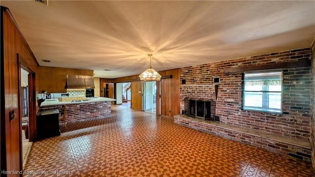 unfurnished living room with wooden walls, tile patterned floors, a fireplace, and brick wall