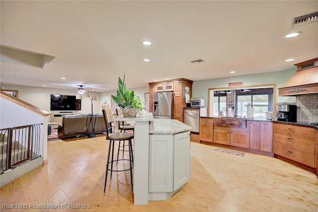 kitchen featuring light stone counters, stainless steel appliances, visible vents, light wood finished floors, and tasteful backsplash