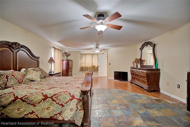 bedroom with stone finish floor, ceiling fan, a textured ceiling, and baseboards