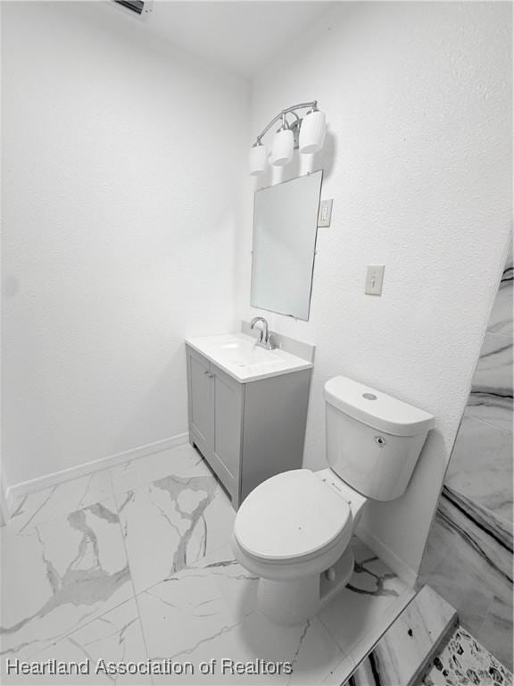 bathroom with toilet, marble finish floor, vanity, and baseboards