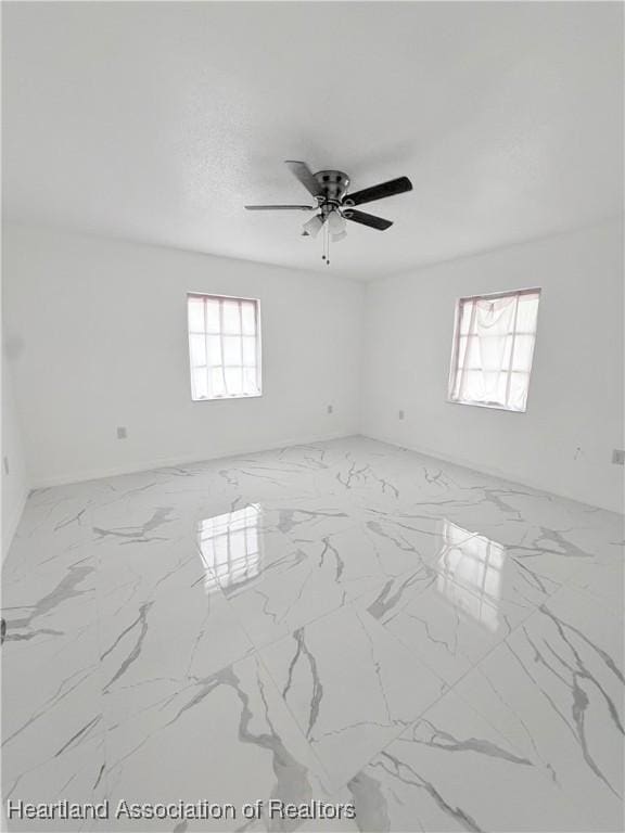 empty room featuring a ceiling fan and marble finish floor