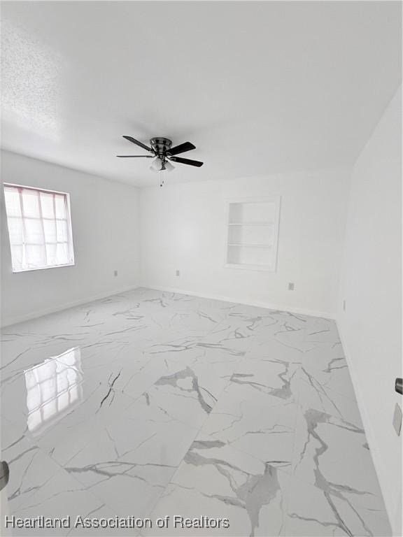 spare room featuring marble finish floor, a textured ceiling, and baseboards