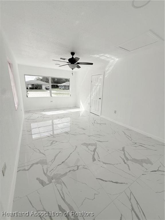 empty room with a textured ceiling, marble finish floor, a ceiling fan, and baseboards