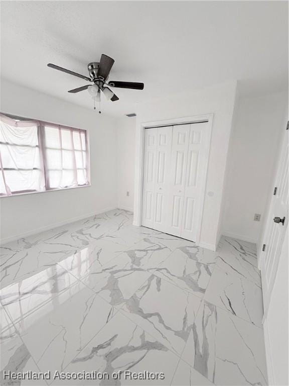 unfurnished bedroom with marble finish floor, a closet, and baseboards