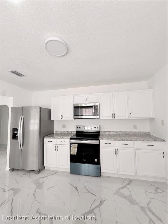 kitchen featuring marble finish floor, stainless steel appliances, visible vents, white cabinets, and a textured ceiling