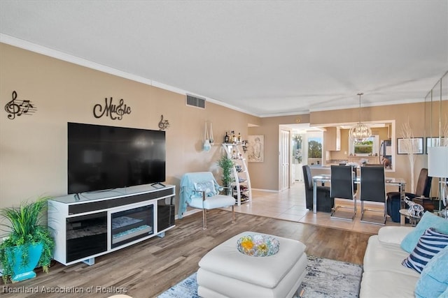 living room featuring ornamental molding, visible vents, a notable chandelier, and wood finished floors