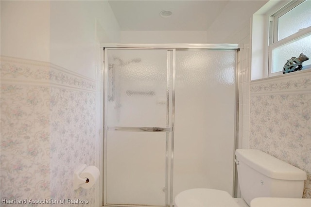 bathroom with a wainscoted wall, a shower stall, toilet, and wallpapered walls