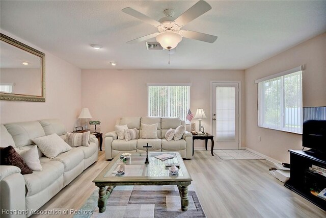 living area featuring light wood finished floors, a ceiling fan, baseboards, and a wealth of natural light