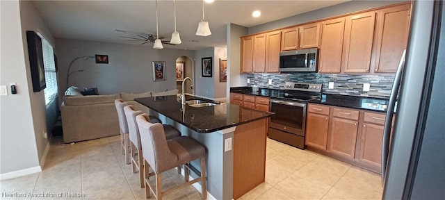 kitchen with a kitchen bar, stainless steel appliances, a kitchen island with sink, sink, and decorative light fixtures