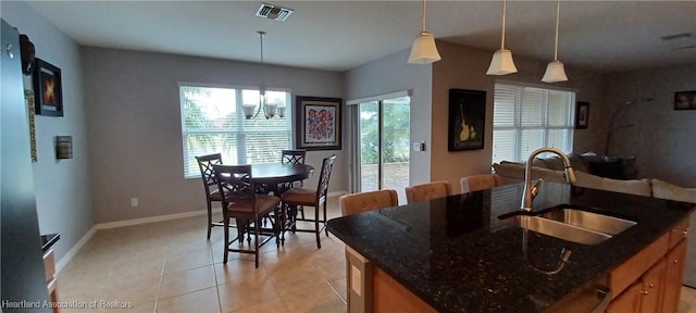 kitchen with sink, dark stone countertops, a chandelier, hanging light fixtures, and an island with sink