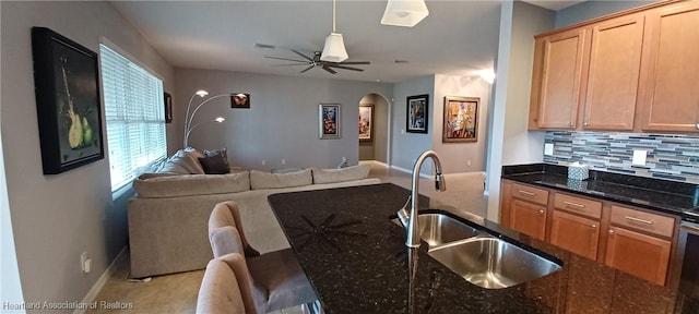 kitchen with decorative backsplash, ceiling fan, sink, and dark stone counters