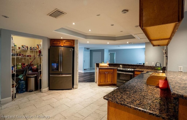 kitchen featuring dark stone counters, a raised ceiling, sink, appliances with stainless steel finishes, and kitchen peninsula