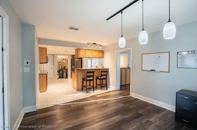 kitchen featuring light brown cabinetry, stainless steel refrigerator with ice dispenser, dark hardwood / wood-style flooring, pendant lighting, and a breakfast bar area