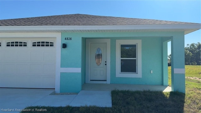doorway to property featuring stucco siding, driveway, a shingled roof, and an attached garage