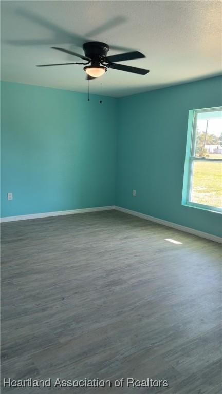 empty room featuring a ceiling fan, wood finished floors, baseboards, and a textured ceiling