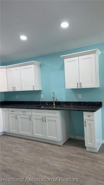 kitchen with light wood finished floors, dark stone counters, recessed lighting, white cabinetry, and a sink