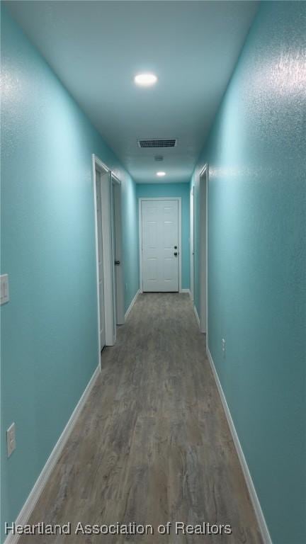 hallway with baseboards, visible vents, and wood finished floors