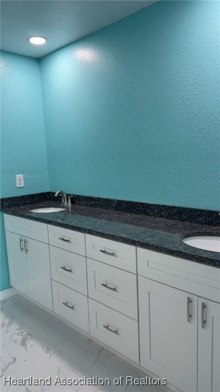 bathroom with marble finish floor, a sink, a textured wall, and double vanity