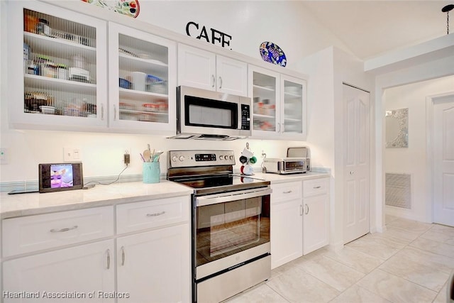 kitchen with appliances with stainless steel finishes, light tile patterned floors, white cabinetry, and light stone counters