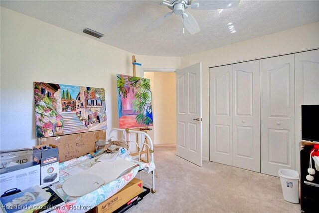 bedroom with ceiling fan, a closet, light carpet, and a textured ceiling